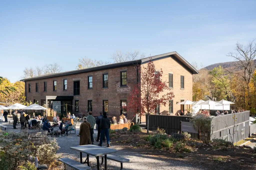 Brick building with outdoor patio seating, umbrellas, and visitors on a sunny autumn day.